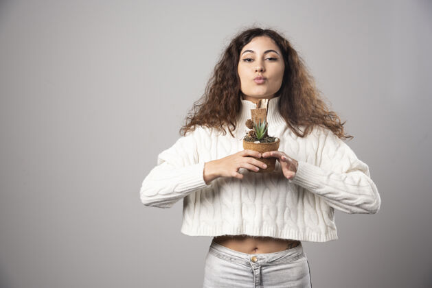 自然在灰色的墙上拿着植物的年轻女子高质量的照片女士脸花盆