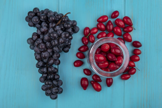 新鲜红色和新鲜的山茱萸浆果在玻璃罐上的俯视图 蓝色木制背景上有黑葡萄黑色浆果罐子