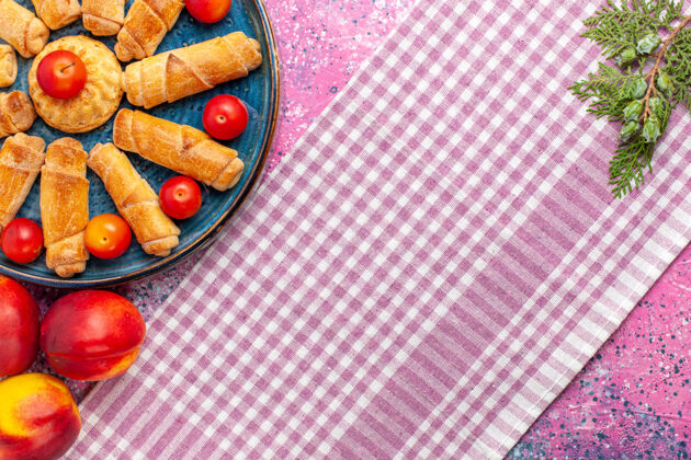 晚餐顶视图甜美美味的百吉饼在托盘里 李子和桃子放在浅粉色的桌子上餐桌子里面