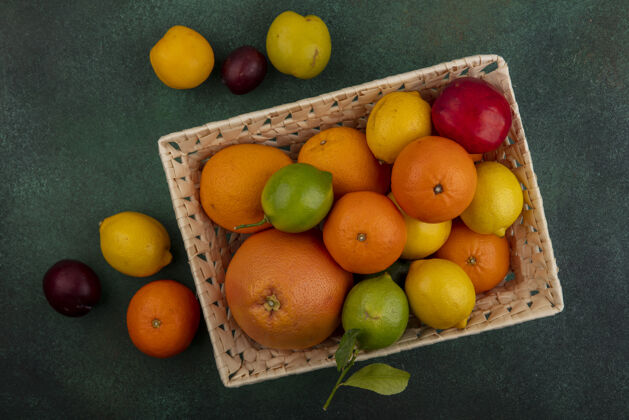 李子在绿色的背景下 一个篮子里放着桃子和柠檬 酸橙 李子 葡萄柚和橙子食物酸橙篮子