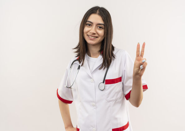 公民年轻的女医生穿着白大褂 脖子上戴着听诊器 站在白墙上微笑着指着第二个手指女人周围人