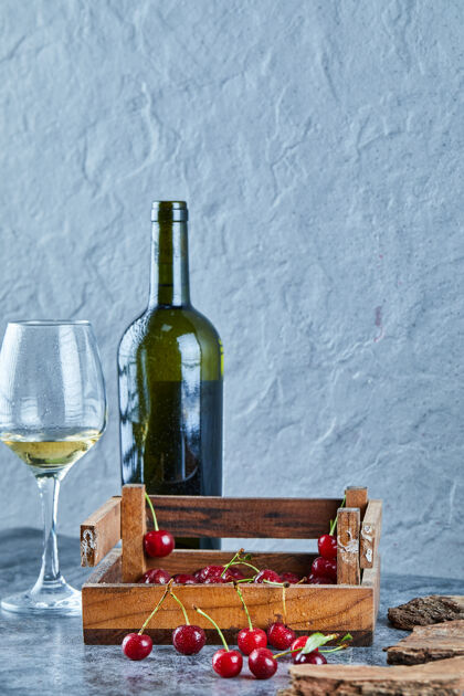 叶子一杯白葡萄酒 一瓶樱桃 一个装在蓝色表面的木盒有机美味多汁
