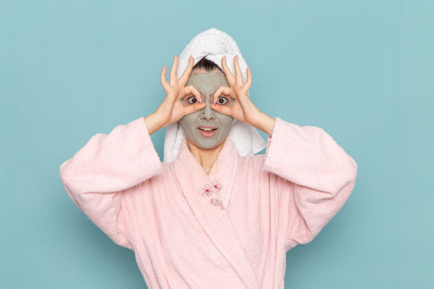 人正面图沐浴后穿着粉色浴袍的年轻女性在蓝色墙壁上摆出有趣的姿势清洁美丽干净的水自我护理霜淋浴视图后面浴袍