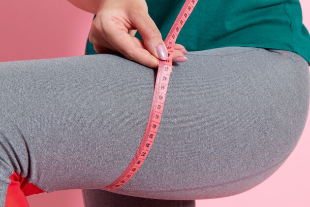 扣件前视图身着绿色t恤的年轻女性在粉色墙上测量她的尺寸腰部运动锻炼美丽苗条运动员手年轻人锻炼