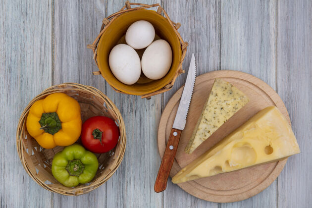 架子俯瞰荷兰奶酪片与刀架上的甜椒和鸡蛋在灰色的背景食物小刀胡椒