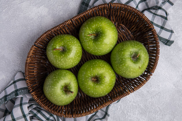 食物俯瞰绿色格子毛巾上篮子里的绿色苹果上衣苹果格子