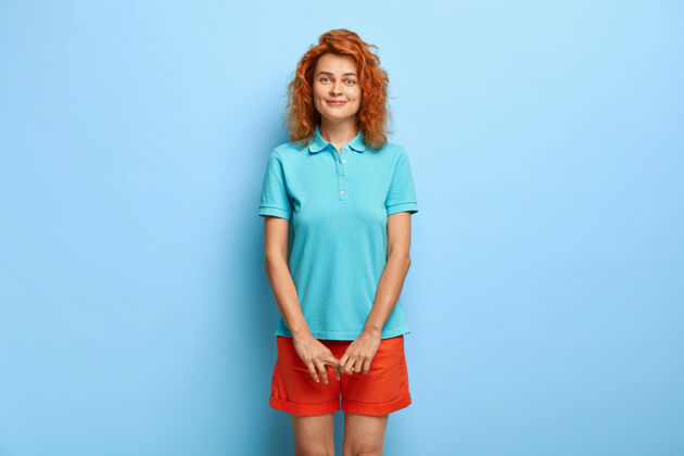爱情端庄可爱的少女 红色卷发 有着满意的表情 穿着休闲的蓝色t恤和短裤酒窝情感空闲时间