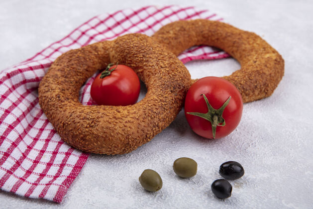 风景白色背景上的红色格子布上 放着新鲜西红柿和橄榄的柔软传统土耳其百吉饼的俯视图新鲜的软的早餐