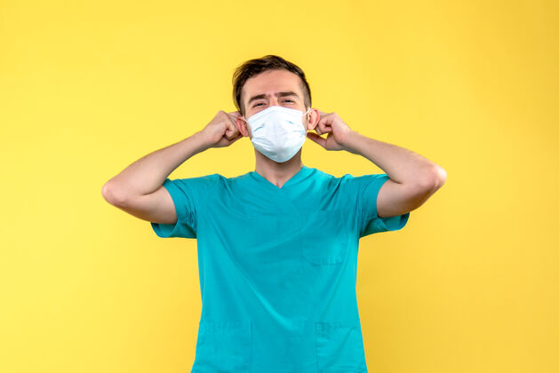 健康黄色墙上戴着无菌口罩的男医生的正视图医学正面成人