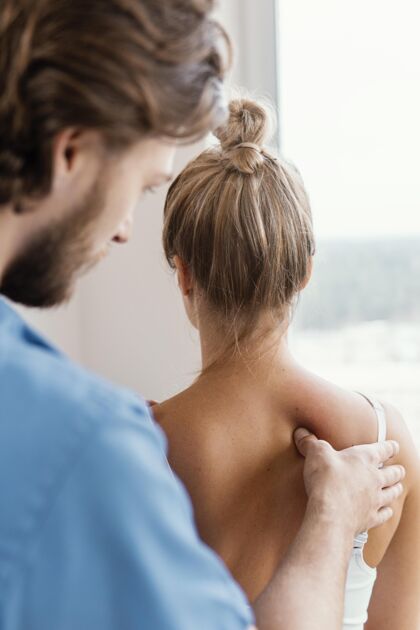 男人男性骨科治疗师检查女性患者脊柱的侧视图女人运动医生