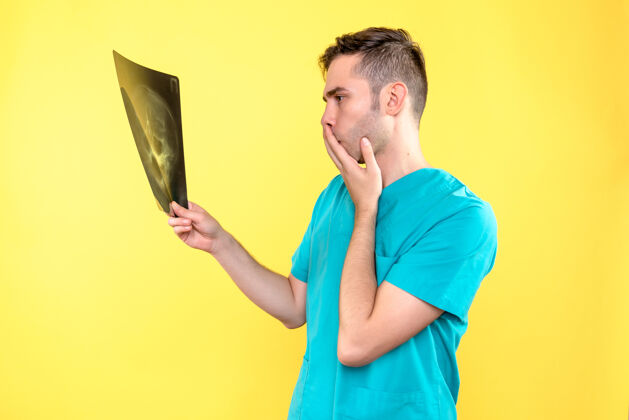 医疗黄色墙上手持x光片的男医生的正视图成人肖像帅哥