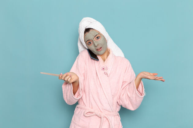 年轻正面图年轻女性穿着粉色浴袍淋浴后在蓝色墙上讲电话美容水自理淋浴干净淋浴表演后面