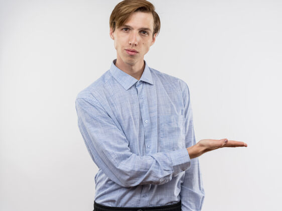 手臂身穿蓝色衬衫的年轻人站在白色的墙上 用手臂展示着什么 他自信的表情男人站姿表情