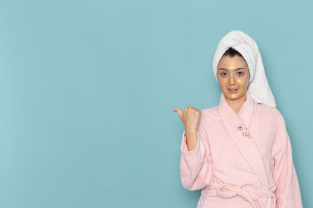 视图正面图身着粉色浴袍的年轻女性淋浴后微笑在蓝色墙壁上美丽的水霜自助淋浴浴室浴室年轻人人