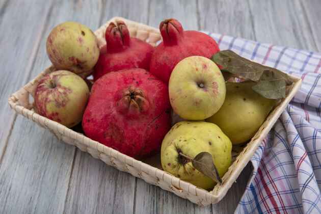 石榴健康水果的顶视图 如石榴 苹果和木瓜 在灰色背景的格子布上放在桶上苹果木瓜水果
