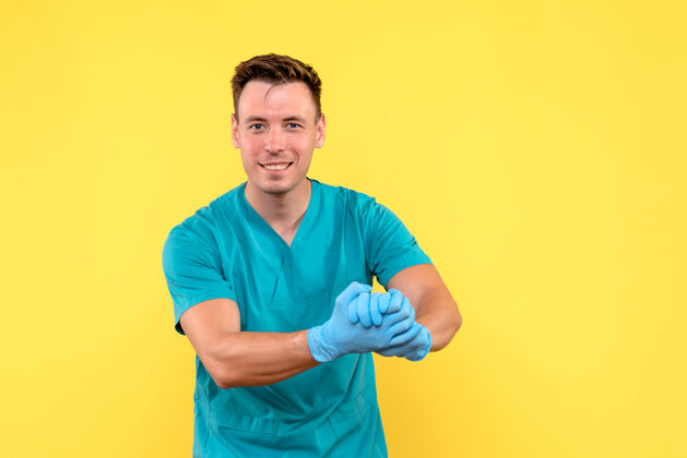 正面黄墙上戴着蓝手套的男医生的正视图微笑医学成人