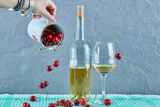 酒女人手上扔着一杯樱桃和一瓶白葡萄酒 杯子放在蓝色的表面上杯子瓶子手