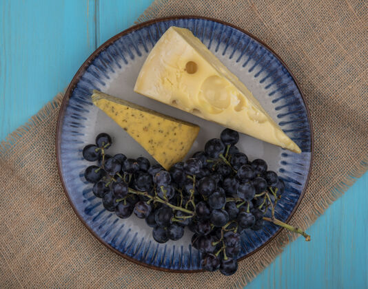新鲜顶视图黑葡萄和奶酪片放在米色餐巾上的盘子里视野葡萄黑色