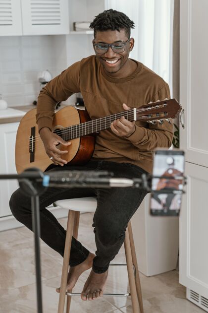 技能笑脸男音乐家在家里弹吉他和智能手机录音的正面图熟练程度房子艺术家