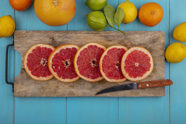 绿松石俯视图葡萄柚楔形物在切割板上用刀和柠檬与青绿色背景上的石灰和橙色楔形视图酸橙