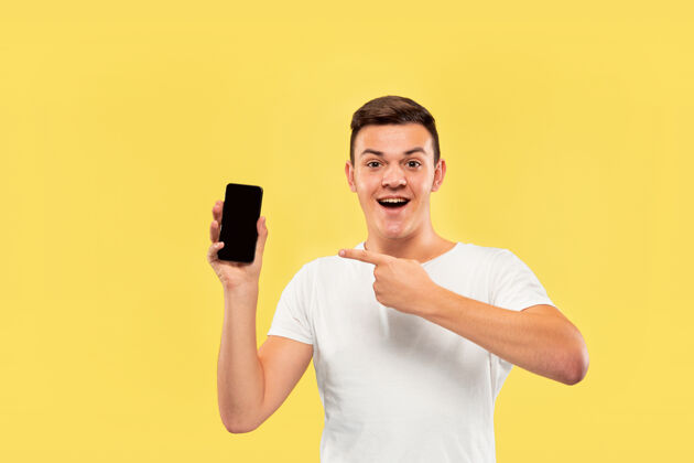 工作黄色工作室背景上的白人年轻人半身肖像穿着衬衫的漂亮男模人类情感的概念 面部表情 销售 广告展示手机屏幕和微笑成人工作肖像