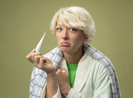感觉生病的不健康的女人 短发裹在毯子里 身体不适 拿着体温计 表情悲伤 患流感 站在光墙上痛苦生病不健康