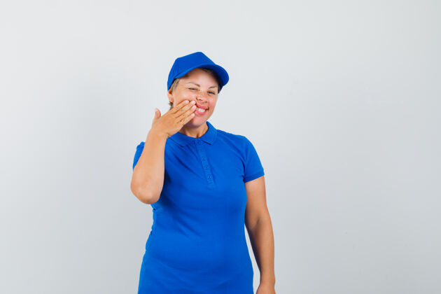 女性穿着蓝色t恤的成熟女人把手按在脸颊上 看起来很高兴帽子活跃可爱
