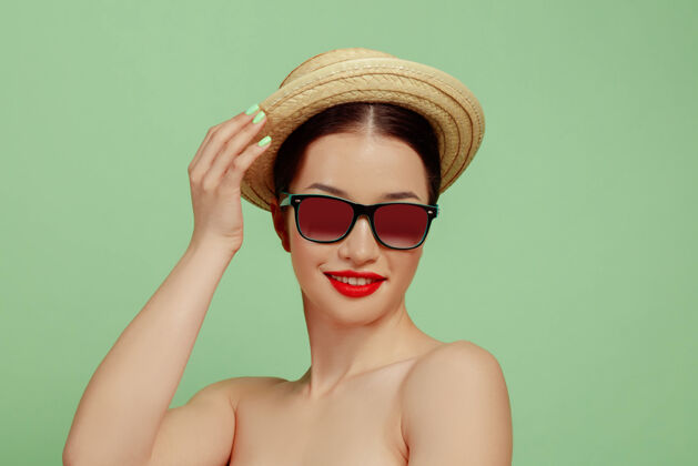 明亮美丽女人的肖像 明亮的妆容 帽子和太阳镜在绿色的工作室背景上时髦和时尚的制作和发型夏天的颜色美丽 时尚和广告概念微笑发型太阳镜新鲜