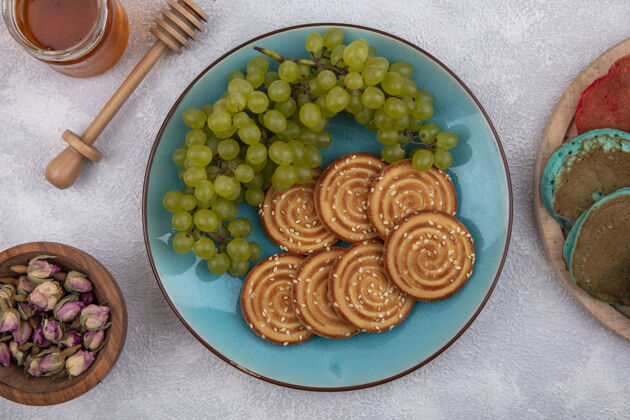 蜂蜜蓝色盘子上放着绿色葡萄 白色背景上放着蜂蜜和干芽 俯视着饼干蓝色食物饼干