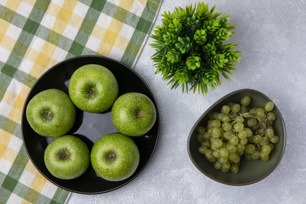 葡萄顶视图绿色的葡萄在一碗绿色的苹果与绿黄色格子毛巾在白色的背景食物绿色顶部