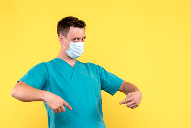 男性黄墙上戴着口罩的男医生的正视图表情穿着医院