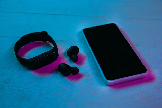 设备紫色霓虹灯和蓝色背景下的一组小玩意的俯视图木制桌子上的智能手机 智能手表和无线耳机广告的复制空间科技 现代 小玩意渐变持有网络