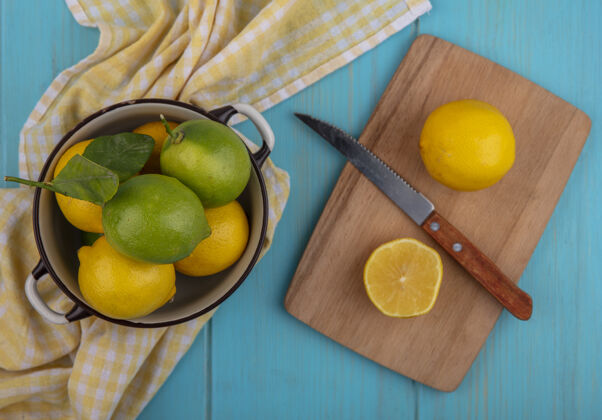 刀上图：柠檬和石灰放在平底锅里 刀子放在砧板上 黄色格子毛巾放在绿松石背景上板水果毛巾