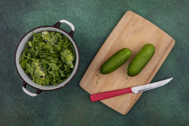 风景顶视图绿色与黄瓜在切菜板上用一把刀在绿色背景的平底锅刀板切割