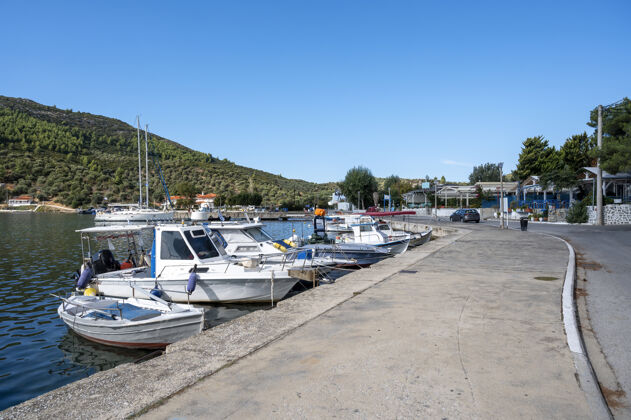 港口停泊在河堤附近的船街上有建筑物和餐馆 绿树成荫 绿山成荫 希腊传统的帆船观点