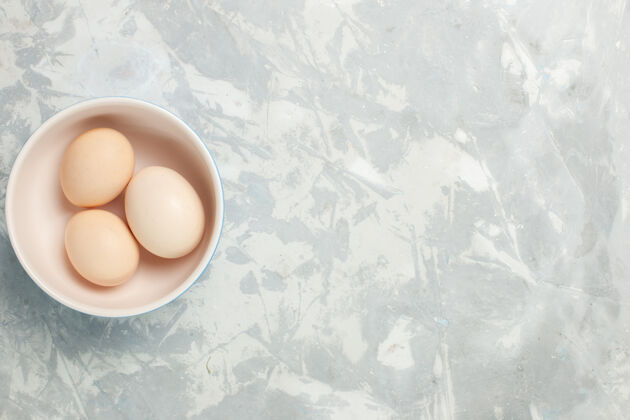 视图顶视图生全蛋在浅白桌子上的小盘子里生食早餐照片早晨背景少量盘子