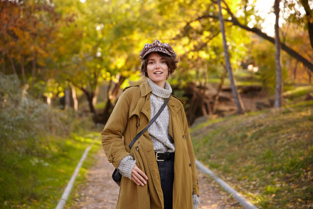 休闲时尚年轻漂亮的棕色头发的女人鲍勃发型穿着时髦的驼色外套 针织圆领衫和豹纹帽子 而站在城市花园化妆印花年轻