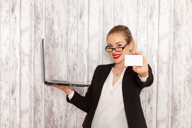 办公室正面图：穿着黑色夹克 穿着严苛衣服的年轻女商人用她的笔记本电脑 在白色表面上拿着名片电话女工作