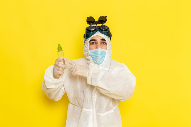 男正面图身着特殊防护服的男科学工作者手持喷雾瓶在浅黄色表面烧瓶实验室外套工人