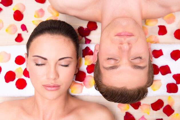 水疗美丽的年轻夫妇躺在玫瑰花瓣里放松年轻花瓣皮肤护理