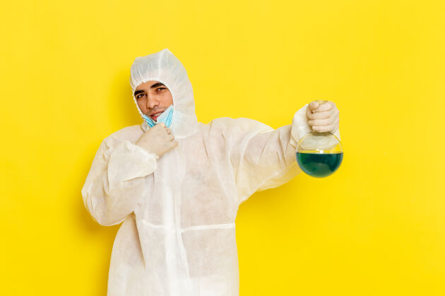 化学正面图穿着特殊防护服的男科学工作者拿着黄色表面上有蓝色溶液的烧瓶套装医生特殊