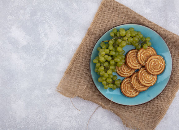 食物顶视图复制空间绿色葡萄和饼干在一个蓝色的盘子上米色餐巾在白色的背景米色复制植物
