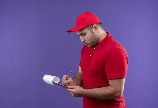 帽子年轻的送货员穿着红色制服 戴着帽子 脸严肃地站在紫色的纸上写着字站立制服人