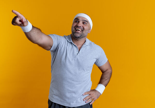 看戴着头巾的成熟的运动型男人看起来很自信 微笑着用手指着站在橙色墙上的一边男人公动装