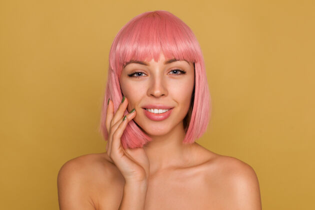发型美丽的年轻积极的女性肖像 粉红色的鲍勃发型 表情平静 举手贴着脸颊 在芥末墙上摆姿势情感表情女士