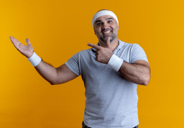 男人戴着头巾的成熟的运动型男人看起来很自信 手指指向侧面 手臂站在橙色的墙上指点教练运动