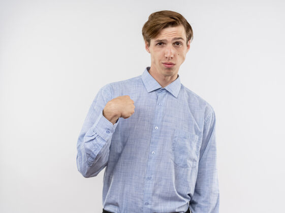手指穿着蓝色衬衫的年轻人看着摄像机 用食指指着站在白色背景下的自己 看上去很自信衬衫立场指向