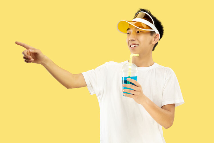 巴塞罗那黄色工作室背景上的韩国年轻人半身像穿着白衬衫 戴着黄色帽子的男模喝鸡尾酒人类情感的概念 表达 夏天 假期 周末舞蹈看惊喜