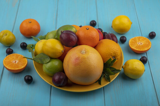 壁板侧视图水果混合在盘子上橙子樱桃李子葡萄柚柠檬柠檬和李子在绿松石背景上食物樱桃李子