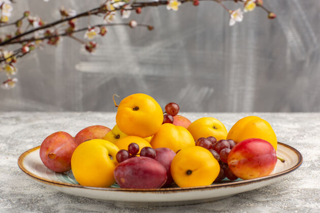 杏子白色桌子上的盘子里放着新鲜甜美的杏子 李子和葡萄李子甜浆果